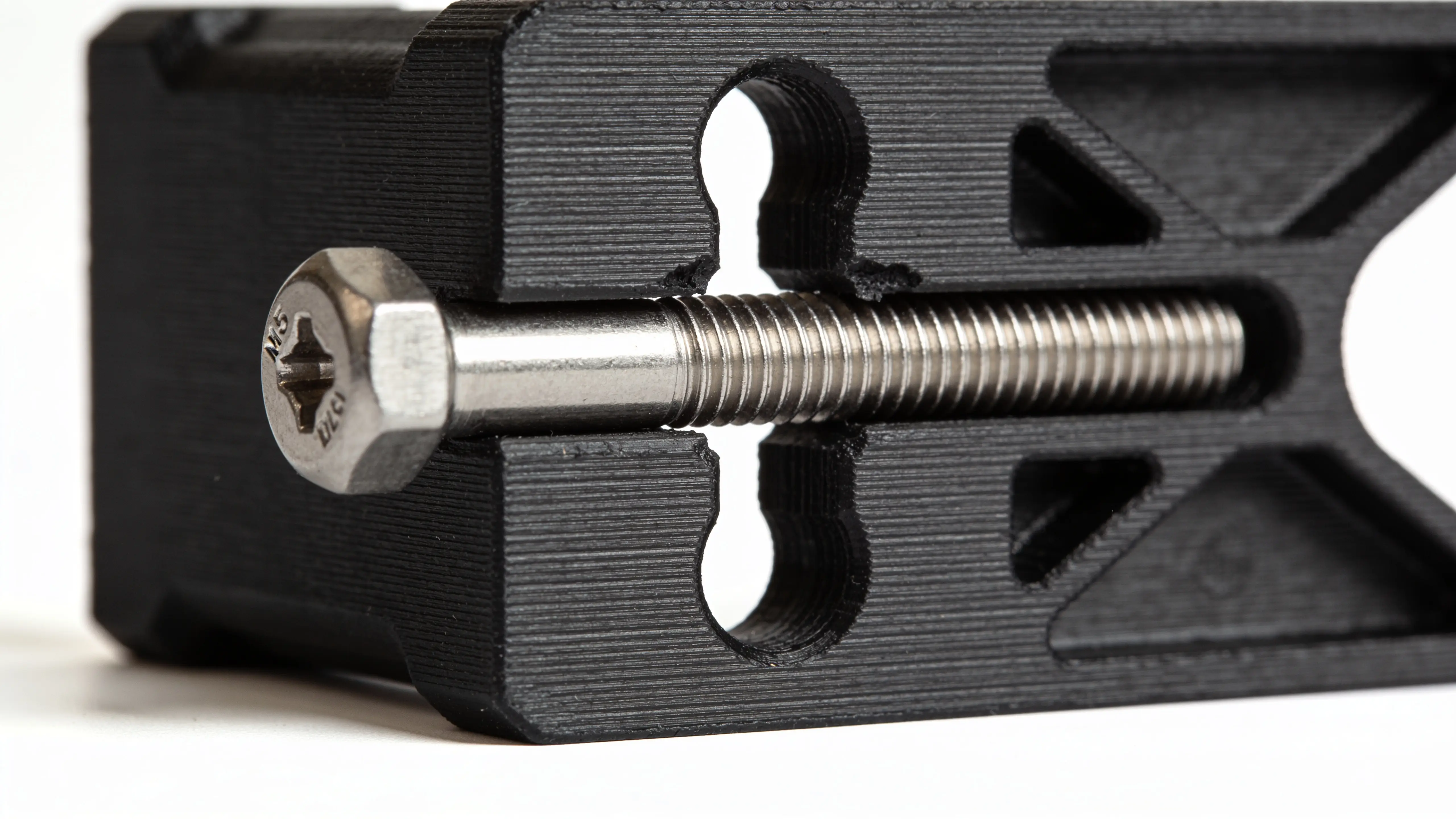 Black 3D printed engineering bracket with a horizontal bolt hole and a stainless steel M5 bolt being inserted — showing slight ovaling at the top of the hole