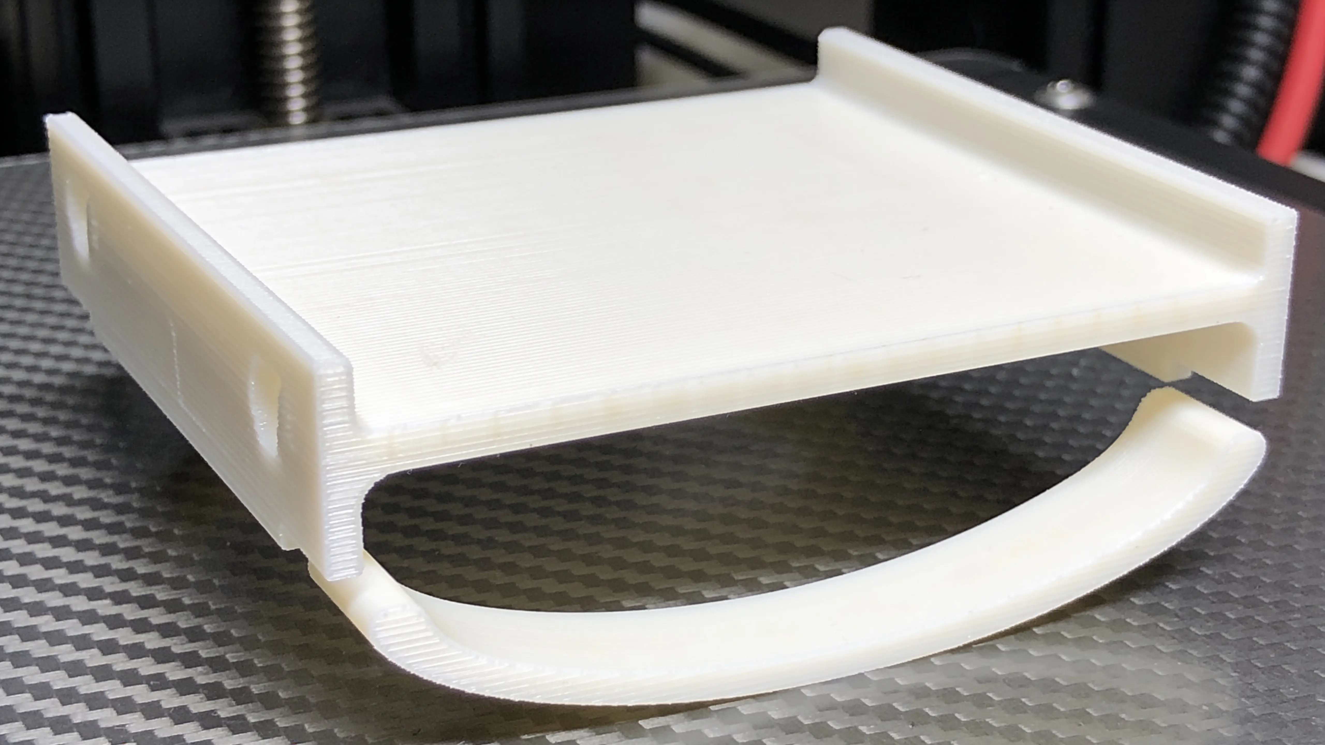 Finished white PLA 3D print on a gray PEI bed showing classic banana-shaped warping deformation with both corners curled upward — what warping looks like